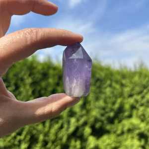 Amethyst Naturstein in der Hand vor grünen Büschen und blauem Himmel