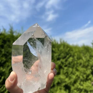 Große Bergkristallspitze in der Hand vor grünem Hintergrund und blauem Himmel