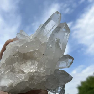 Bergkristall Stufe in der Hand vor strahlendem Himmel und grünen Büschen
