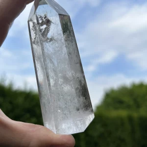 Bergkristall Spitze in einer Hand vor Himmel mit Wolken und grünen Büschen