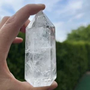 Kristallspitze aus Brasilien vor grünem Busch und Himmel