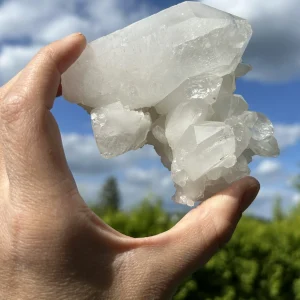 Bergkristall-Stufe zwischen Fingern, fotografiert vor blauem Himmel