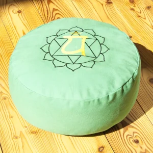 Herzchakra Meditationskissen mit gesticktem Chakrasymbol auf grünem Bezug, fotografiert auf Holzuntergrund